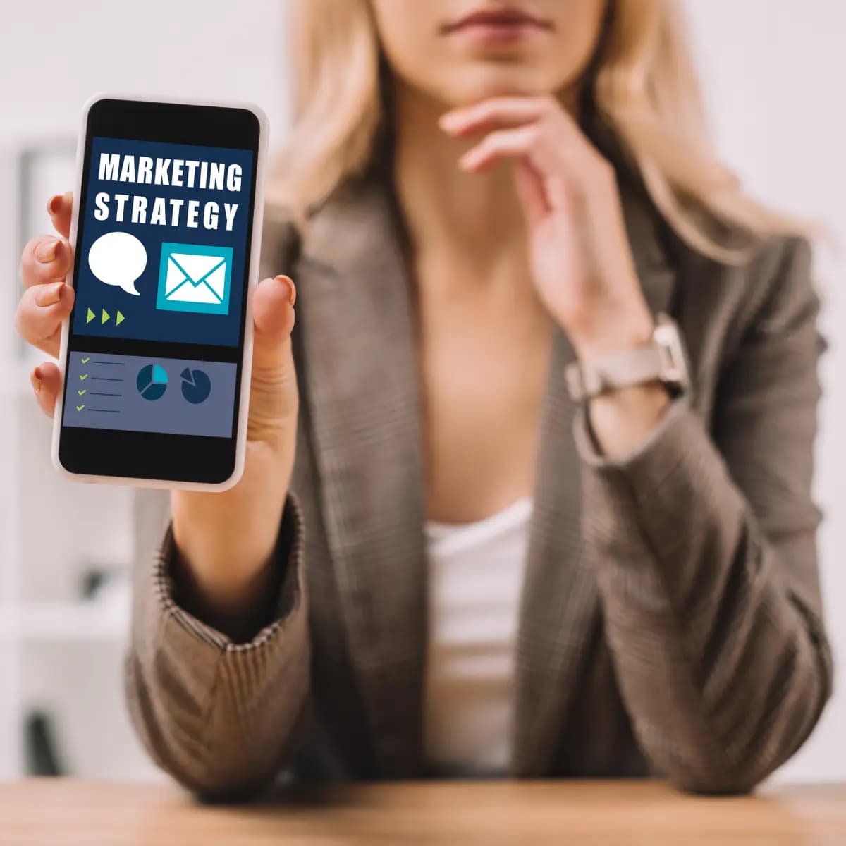 A businesswoman holding up a smartphone with the word marketing strategy on it, aiming to elevate her premium business.